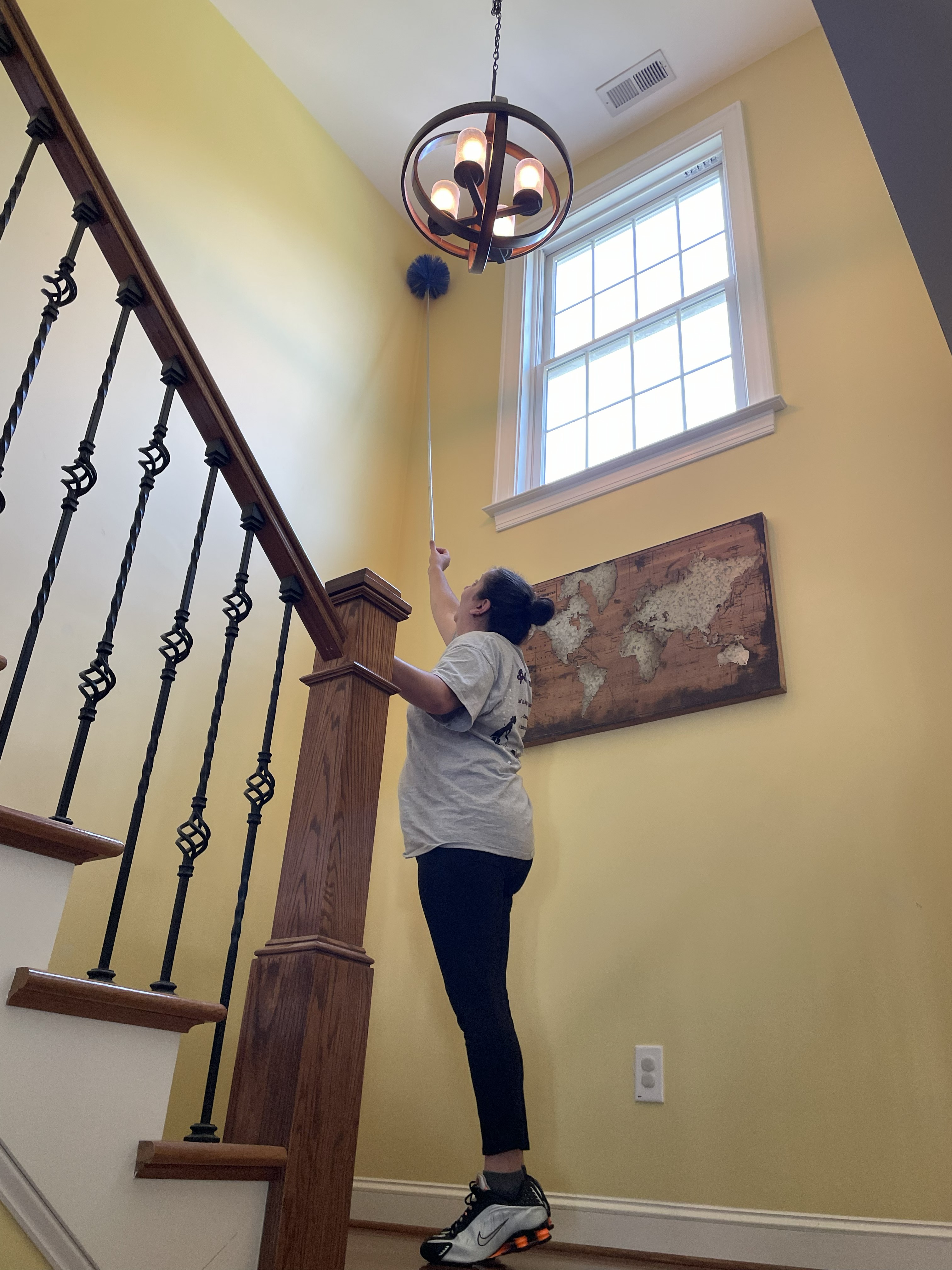 Professional cleaner dusting high fixtures in a residential home